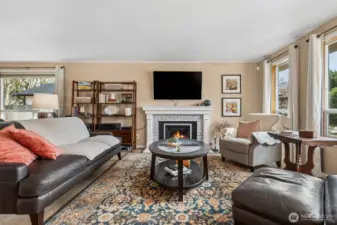 There’s something very satisfying about a living room that feels balanced the second you walk in. The brick wrapped gas fireplace anchors the space with a bit of texture and personality, topped by a classic white mantle that feels timeless instead of trendy. The TV mount above makes the setup effortless, no measuring tape drama required. Sunlight filters through the pair of front windows and that larger picture window near the dining area, giving the room a soft, lived in glow throughout the day. Wrapped in those creamy latte toned walls, the whole space feels warm, inviting, and ready to host everything from quiet evenings to full house gatherings.