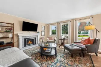 This perspective shows off the scale of the living room in a really satisfying way. The trio of large windows pulls your eye outward toward the front yard, filling the space with natural light and giving that open, airy feeling buyers are always hoping for. Thoughtful window design allows the lower sections to lift for ventilation without breaking up the view or cluttering the wall visually. Nearby, the newer gas fireplace anchors the room with warmth and practicality, complete with a built-in blower that helps distribute heat when you want the whole space feeling inviting. The hearth sits neatly in line with the room, keeping walkways clear and furniture options flexible.