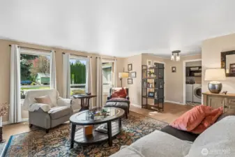Looking back toward the entry from the opposite side of the living room gives you a full sense of how open and functional this space really is. The trio of front facing windows keeps the room feeling bright throughout the day, while the nearby laundry room comes into clearer view, placed exactly where it makes everyday routines easier. Comfort has already been considered here too, with the heat pump set up to deliver cool relief during warmer months and a recently serviced furnace supporting efficient year round living. These are the kinds of updates that quietly make a difference. The overall feel remains relaxed and cohesive, with clean lines, warm wall tones, and a layout that supports both quiet evenings and busier household moments.