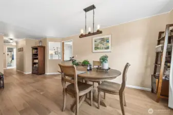 From the dining room window looking back across the space, you really get a sense of how generous and usable this room is. That long uninterrupted wall is practically begging for a statement hutch, buffet, gallery display, or even a sleek bar setup for entertaining nights in. The wide plank engineered hardwood floors carry the same warm, polished vibe seen throughout the main areas, giving the room a grounded, cohesive feel. Off to the right, the doorway into the kitchen keeps everything conveniently connected, while the hallway view in the distance shows how intuitively the home is laid out for everyday living.