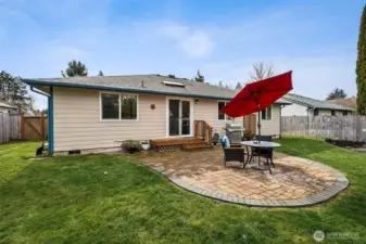 Standing at the edge of the yard and looking back, the layout just makes sense. The slider opens to a petite deck landing that feels like the perfect perch for morning coffee, then steps lead down to the wide paver patio where gatherings naturally unfold. Lawn runs along both sides of the home, giving pets, play, or garden plans plenty of room to happen. The exterior palette of soft cream with moody blue trim feels very Pacific Northwest chic, and those white vinyl windows are the practical heroes here, durable, easy to care for, and great at helping manage comfort and efficiency inside.