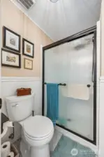 Tucked just off the vanity area, the primary suite water room keeps things private and practical in the best way. More beadboard wainscoting continues the charm, paired with those warm latte toned walls that feel calm and easy to live with. A full shower with privacy glass lets the light in while keeping the moment discreet, and the toilet sits comfortably in the same enclosed space for a true en suite setup. Bonus perk, this home has a tankless water heater that has been recently serviced, so long showers, quick rinses, and busy mornings all get along just fine here.