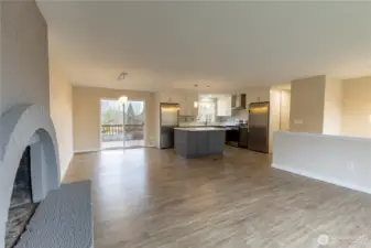 Living room with wood burning fireplace, looking into dining room and kitchen.
