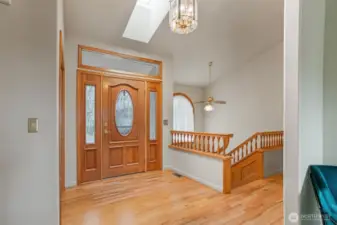 Step into a warm and welcoming foyer filled with natural light from a skylight above, highlighting true oak hardwood floors and elegant millwork.