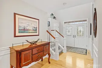 The entry showcases Birch hardwood floors and crisp millwork, creating an immediate sense of refinement as you step inside. The fiberglass double doors with decorative glass panels fill the space with natural light and set an elegant tone for the home.