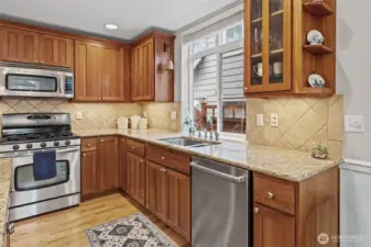 This work zone of the kitchen showcases crown-topped Shaker cherry cabinetry, granite counters, and under-cabinet lighting that brightens the entire space. The window above the sink brings in natural light while highlighting the upgraded Bosch dishwasher and thoughtfully designed storage throughout.