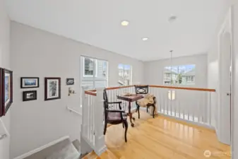 This upper landing creates a bright and comfortable flex space, ideal for reading, relaxing, or working from home. Multiple windows fill the area with natural light, highlighting the open railing design and the home’s warm, inviting atmosphere.