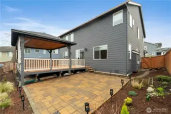 Beautiful backyard with a covered deck overlooking a large patio and tidy landscaping.
