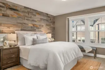 The primary bedroom features a warm wood accent wall and warm paint tones and an oversized picture window.