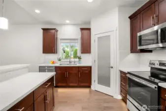 Modern kitchen with stainless steel appliances, quartz countertops, rich wood cabinetry, and a walk-in pantry behind a frosted glass door.