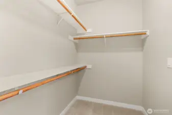 Primary walk-in closet boasts of hanging space and solid wood shelving.