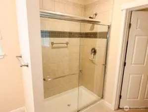 Attractively tiled shower with grab bar, and door to the walk-in closet.