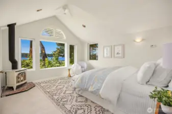 Inviting primary retreat with vaulted ceilings, warm gas stove, and picturesque water views creating a calm and restful setting.