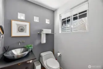 Stylish powder room with modern vessel sink, sleek finishes & designer touches. Window brings in natural light, creating a bright, refreshed feel.