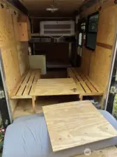 Utility trailer with queen bed in back, storage cubbies, and 2 more single beds in the front. Also has an awning.