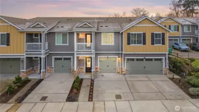 Front exterior featuring attached garage, covered entry, private balcony, and low-maintenance landscaping.