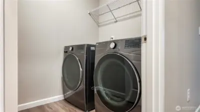 Dedicated laundry room with side by side washer and dryer and upper shelving.