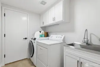 Main-floor utility/laundry room with utility sink, built-in cabinets, and tile flooring, conveniently located off the three car garage.