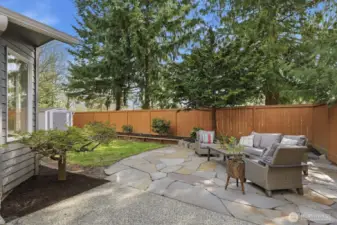 Extended flagstone patio off kitchen/breakfast nook framed by mature landscaping and garden space.