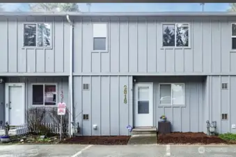 This photo showcases the front exterior view of the condo building, highlighting the assigned, reserved parking space located conveniently in the front. Please note that access to the attached two-car tandem garage is situated around the back of the property.