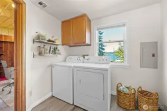 Bright and functional, the laundry room features upper cabinets, open shelving for organization, and a window framing gorgeous Lake Washington views—making chores a little more enjoyable. (Virtually Staged)
