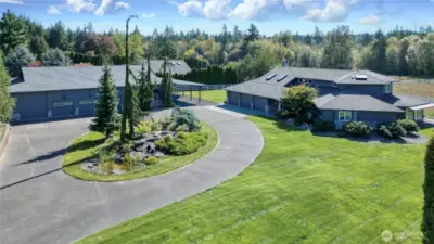 Drone view of front of property, custom 3500+ sq ft home on right, 3000 sq ft shop on left with attached carport. I love the paved circle drive, the massive water feature and Koi in the middle and the Dr. Seuss trees!