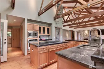 Kitchen view two, the beams and dramatic ceiling continues! To your left is the 4-season covered patio affectionately known as the White Room, down the hall to your left is the furnace room, water heater room and your utility room. We thought the chalkboard paint on those center cabinets was fun :)