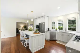 Updated chef’s kitchen with white cabinetry, stainless appliances, oversized island, and abundant windows capturing natural light and territorial views in this Lake Wilderness home.