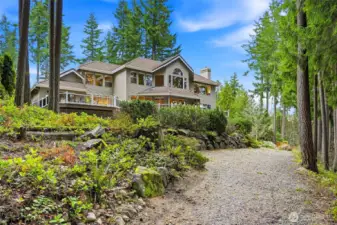 Stunning back elevation with long driveway approach, lush landscaping, and elevated positioning showcasing this luxury Maple Valley lake view home.