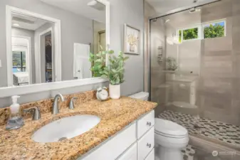 The en-suite bathroom for the primary bedroom features a granite countertop vanity, octagon mosaic tile floors, and tile shower with a rain shower head.