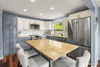 The remodeled kitchen features granite countertops, center island, opaque glass subway tile backsplash, stainless steel appliances, soft-close drawers, and a nearby pantry closet.