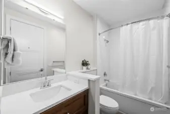 Guest Bathroom in hallway has a pocket door to bedroom.  Deep tub, under vanity lighting and quartz keep this light and bright!