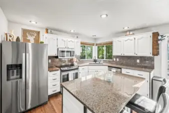 The bright kitchen has hardwood floors, stainless steel appliances, & granite counters