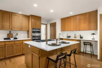 The spacious island offers casual seating, complemented by an adjacent built-in desk area - all with updated quartz countertops.  Just beyond, an oversized walk-in pantry sits near the pocket door leading to the nearby living room.