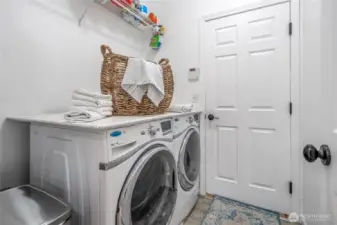 Large pass-through laundry room with storage above and access to the garage beyond.