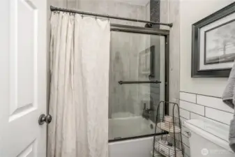 A shower/bath combo unit with glass doors and a window for natural light but high enough for privacy.
