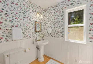 The main floor guest bath features a charming pedestal sink and warm hardwood floors, combining classic style with inviting simplicity.