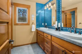 Two full upper-level guest baths, each with heated porcelain tile floors and glass mosaic tile backsplashes.