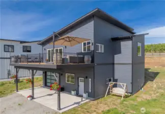 Exterior view of home w/ upper level view deck, a covered lower patio, garage w/ oversized doors & ample parking complete w/ 30amp & septic RV hookups.