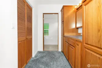 The walkway inside the primary bedroom leading to the ensuite bathroom includes a large walk-in closet, built in cupboards and drawers and a mirror with vanity lighting.