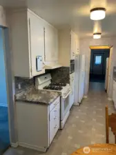 Left side of kitchen with Gas Stove and vent above, microwave Refrigerator, and cabinets