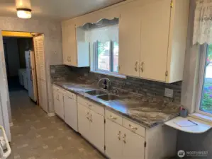 Right side of kitchen has sink dishwasher and Pantry in breezeway on both sides and around corner in Living room. New Counter and tiles. Lots of Cabinets for storage. Looks out to front gardens and driveway.