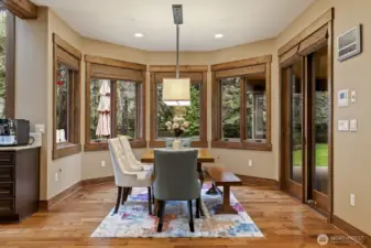 Adjacent informal dining area with wall of windows framing the backyard and doors to the covered outdoor kitchen.