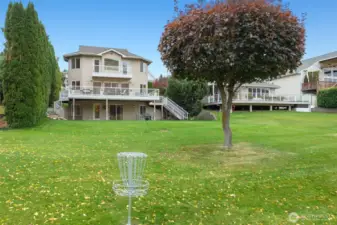 View of the home from the shared greenspace, showcasing the upper and lower decks and easy access to the waterfront.