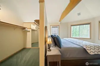 Spacious walk-in closet in the primary suite offering extensive hanging space, built-in shelving, and direct connection to the bright bedroom with vaulted ceilings and exposed beam.
