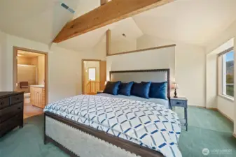 Spacious primary bedroom with vaulted ceilings, exposed beam detail, and direct en suite access. Features soft natural light and peaceful views of the surrounding landscape.