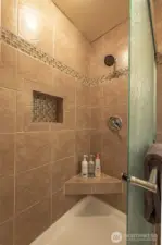 Beautifully tiled walk-in shower with glass door, built-in niches, and accent tile detailing — a clean, upgraded feature of the primary bathroom.