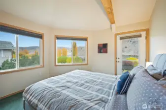 Comfortable upper-level bedroom with large windows overlooking the lake, exposed beam detail, and plush carpeting. A restful space with abundant natural light.