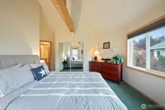 Light-filled upper bedroom with vaulted ceilings, mirrored closets, and serene views of the surrounding landscape. A quiet retreat with easy deck access.