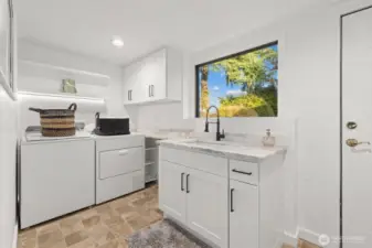 Proper laundry room with updated cabinetry, quartzite countertops, floating shelves and hardware. door leads out to backyard area.